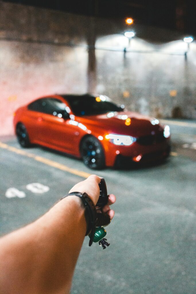 A hand holding keys unlocking a red luxury car parked at night