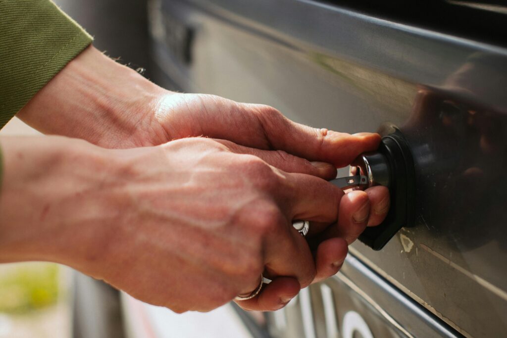 Close-up of hands unlocking a vehicle trunk with a key, showing detail and reflection.